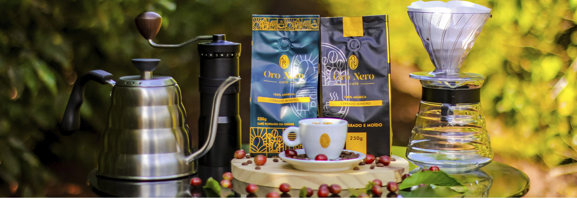 Cafés Oro Nero em grãos e moído, xícara e utensílios de preparo em uma mesa no jardim